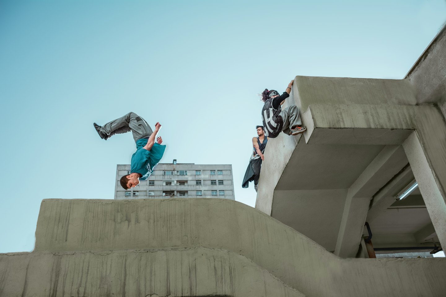 Tre uomini fanno parkour vicino a una struttura urbana in cemento.